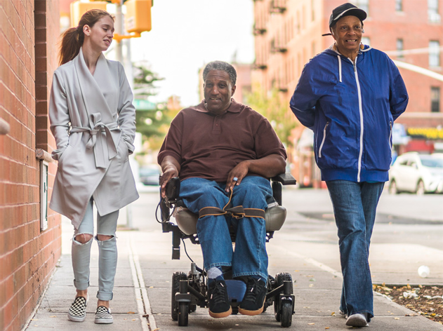 A group of people travelling through a city together. Some of them have disability.