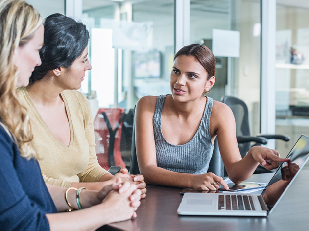 A person explaining something on a laptop to 2 other people in an office.