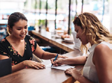 2 people at a desk. One of them is writing on a document.