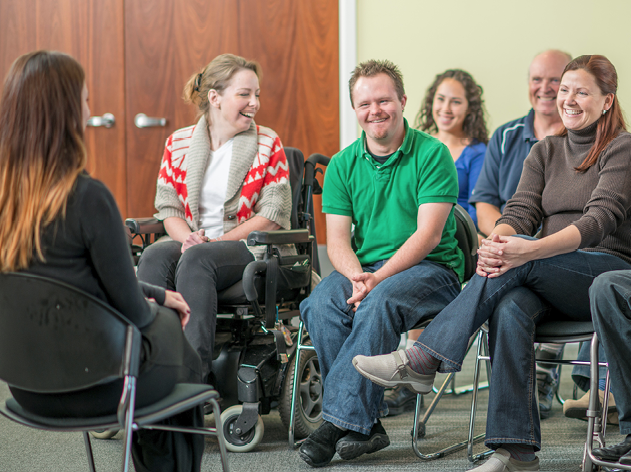 A person talking to a group of people from the community. Some of the people have disabilities.