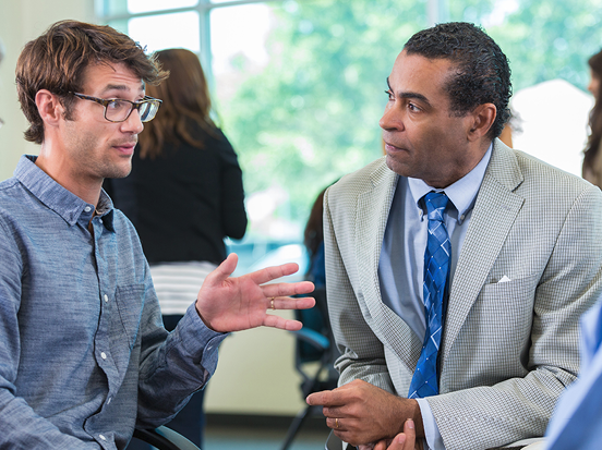 2 people having a conversation in an office.